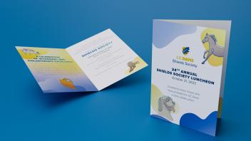 Two bi-fold Shields Society Invitation cards sitting on a blue surface.