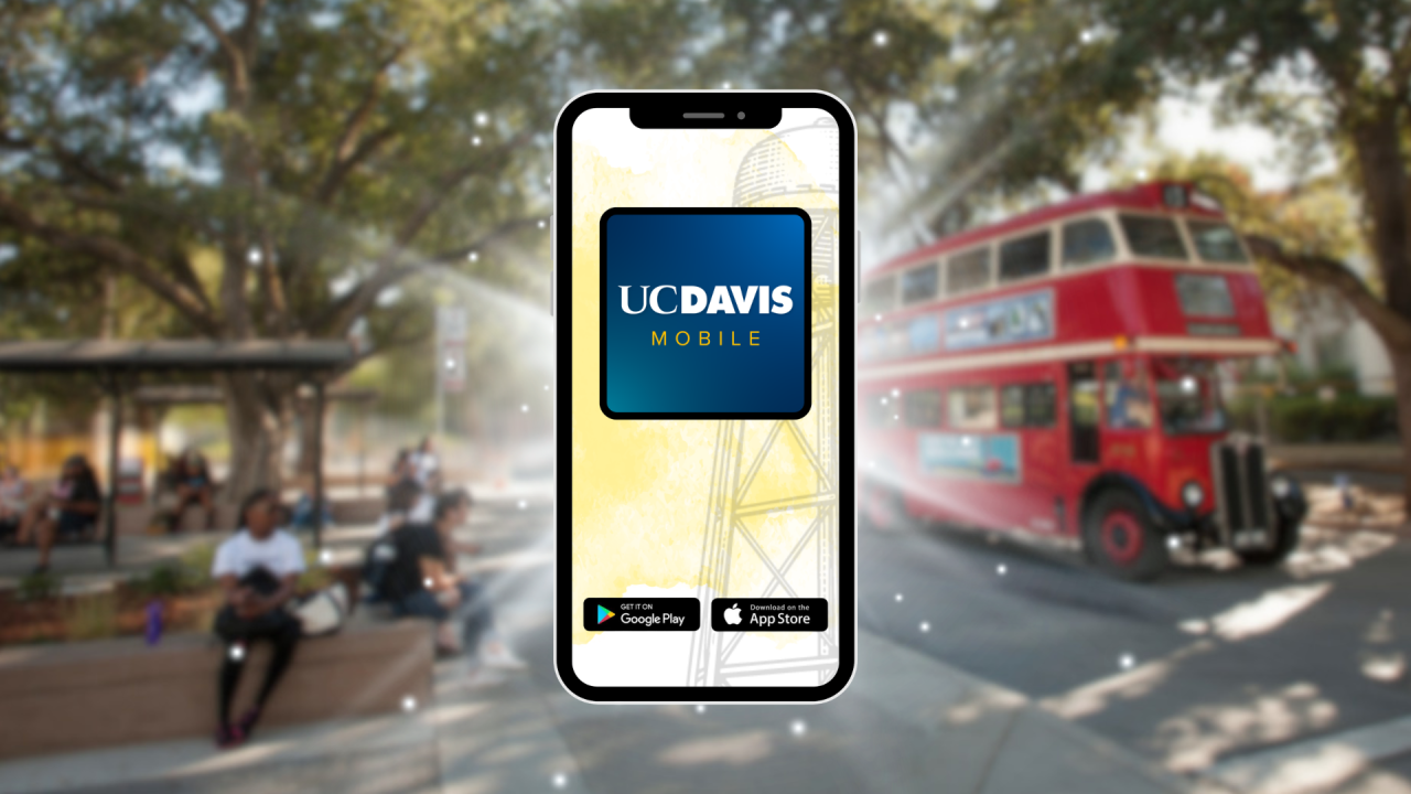 Phone displaying UC Davis Mobile app, blurred campus quad with students and red double-decker bus